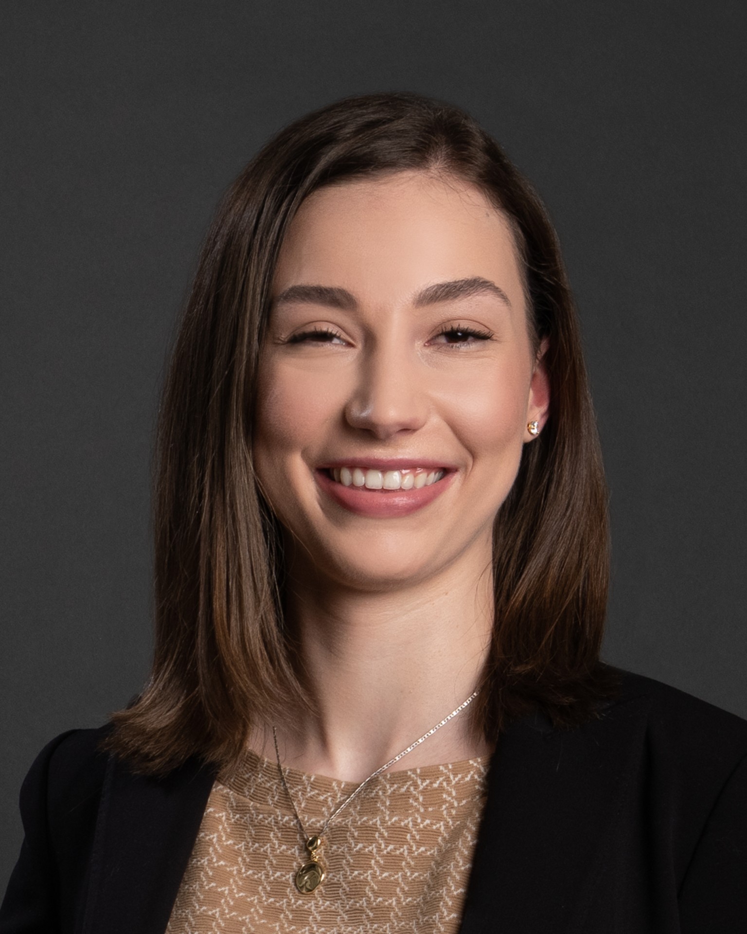 A professional headshot of a smiling woman with shoulder-length brown hair, wearing a black blazer and a lace top.